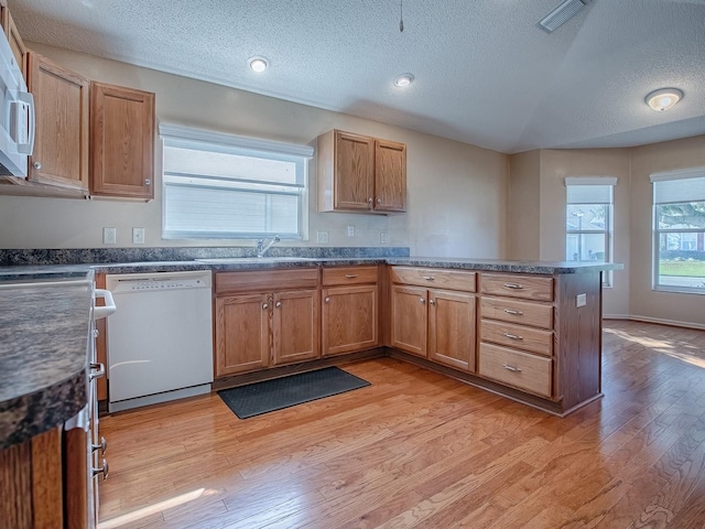 kitchen with white appliances, kitchen peninsula, a textured ceiling, light hardwood / wood-style flooring, and sink