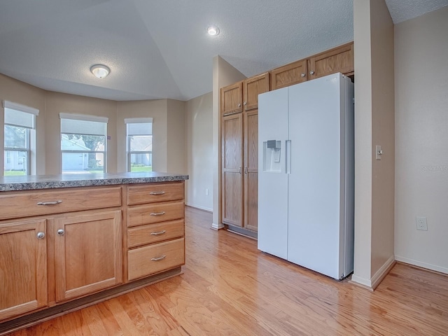 kitchen featuring white fridge with ice dispenser, a textured ceiling, light wood-type flooring, and lofted ceiling