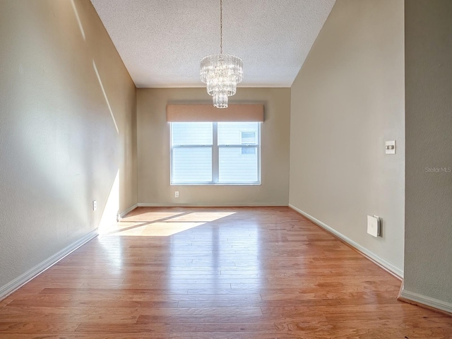 empty room featuring an inviting chandelier, light wood-type flooring, and a textured ceiling