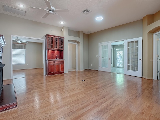 unfurnished living room featuring light hardwood / wood-style flooring, ceiling fan, sink, and a textured ceiling