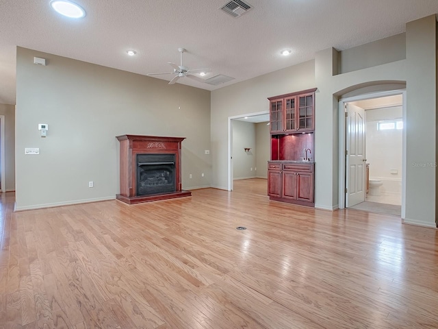 unfurnished living room featuring light wood-type flooring, a textured ceiling, and ceiling fan