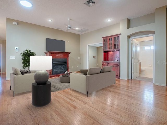 living room with ceiling fan, a textured ceiling, sink, and light hardwood / wood-style floors