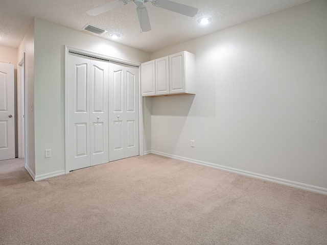 unfurnished bedroom with a closet, ceiling fan, light colored carpet, and a textured ceiling