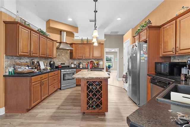 kitchen with pendant lighting, light hardwood / wood-style floors, a kitchen island with sink, wall chimney range hood, and stainless steel appliances