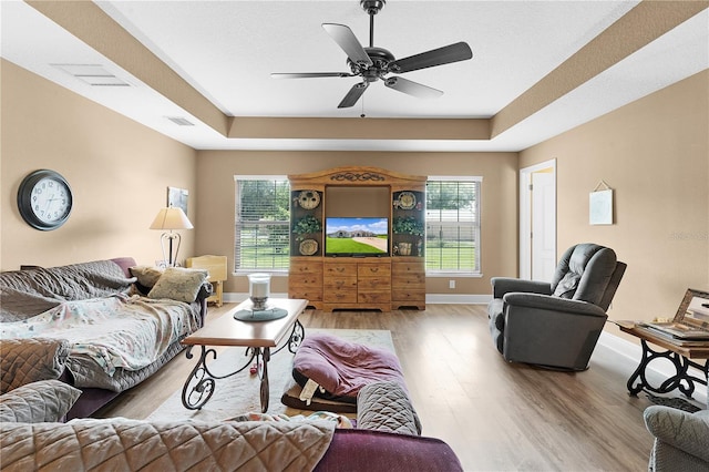 living room featuring light wood-type flooring, a tray ceiling, and ceiling fan