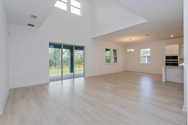 unfurnished living room featuring a towering ceiling, an inviting chandelier, and light hardwood / wood-style flooring