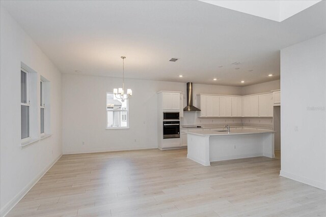 kitchen with wall chimney exhaust hood, a kitchen island with sink, light hardwood / wood-style flooring, and white cabinets