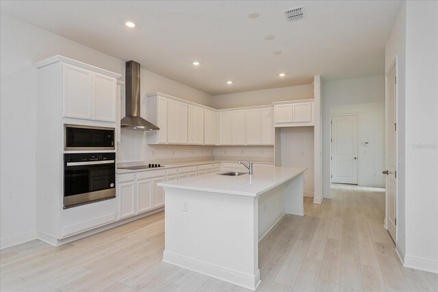 kitchen featuring sink, wall chimney exhaust hood, a center island with sink, black electric cooktop, and stainless steel oven