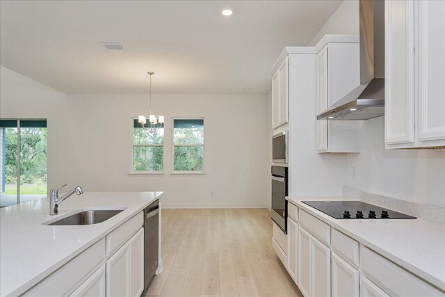 kitchen with appliances with stainless steel finishes, light hardwood / wood-style floors, white cabinetry, sink, and wall chimney range hood