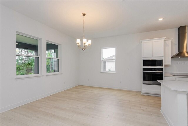 kitchen with stainless steel appliances, white cabinets, plenty of natural light, and wall chimney range hood