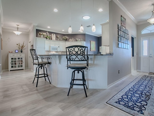 kitchen featuring hanging light fixtures, a breakfast bar, white cabinets, and kitchen peninsula