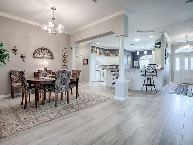 dining area with light hardwood / wood-style floors, a notable chandelier, ornamental molding, and decorative columns