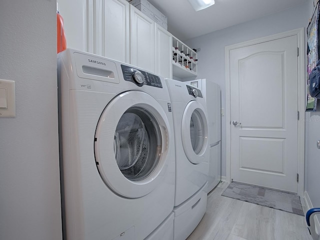 clothes washing area with light hardwood / wood-style floors, cabinets, and washing machine and clothes dryer