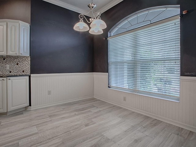 unfurnished dining area with ornamental molding, an inviting chandelier, and light wood-type flooring