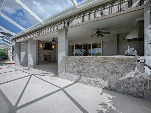 view of patio featuring ceiling fan, glass enclosure, and an outdoor kitchen