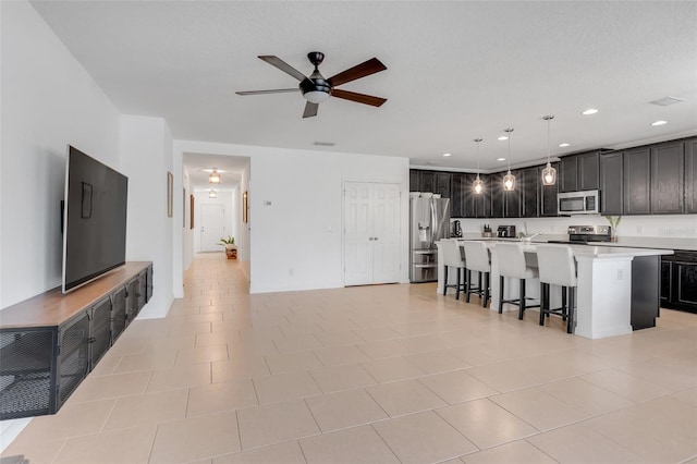 kitchen featuring pendant lighting, light tile patterned flooring, an island with sink, appliances with stainless steel finishes, and ceiling fan