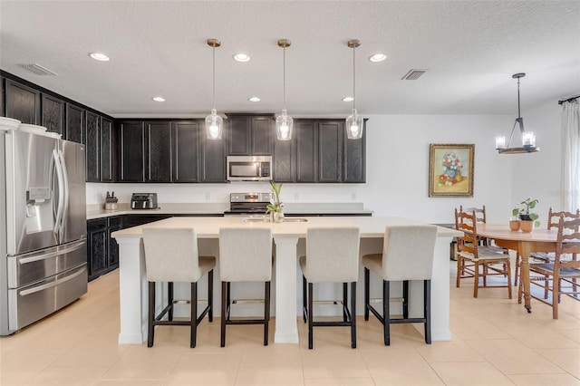 kitchen featuring an island with sink, a breakfast bar, stainless steel appliances, a textured ceiling, and decorative light fixtures