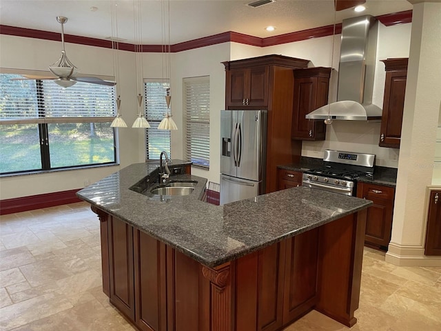 kitchen with an island with sink, pendant lighting, stainless steel appliances, sink, and wall chimney range hood