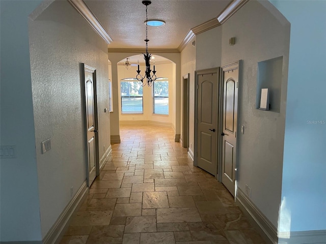 corridor with a textured ceiling, ornamental molding, and an inviting chandelier