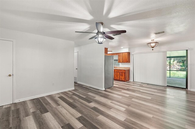 unfurnished living room featuring a textured ceiling, light wood-type flooring, and ceiling fan