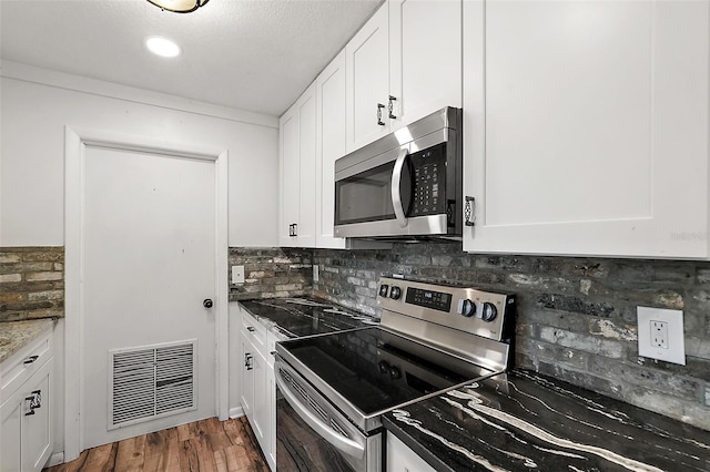 kitchen with backsplash, dark hardwood / wood-style flooring, white cabinets, and appliances with stainless steel finishes