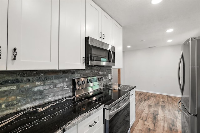 kitchen featuring decorative backsplash, appliances with stainless steel finishes, dark stone counters, light hardwood / wood-style flooring, and white cabinetry