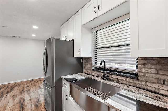 kitchen featuring sink, light stone counters, stainless steel fridge, hardwood / wood-style floors, and white cabinets