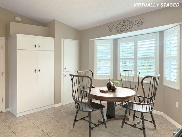 dining space featuring light tile patterned floors, a textured ceiling, and lofted ceiling