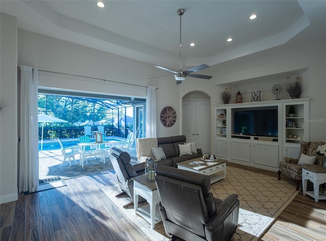 living room with a tray ceiling, light wood-type flooring, and ceiling fan