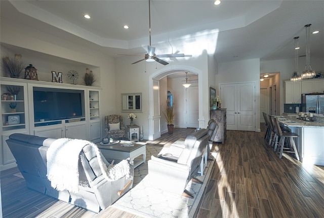 living room featuring a high ceiling, ornate columns, a tray ceiling, ceiling fan, and dark hardwood / wood-style flooring