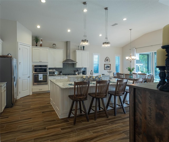 kitchen with wall chimney range hood, white cabinets, hanging light fixtures, appliances with stainless steel finishes, and dark hardwood / wood-style floors