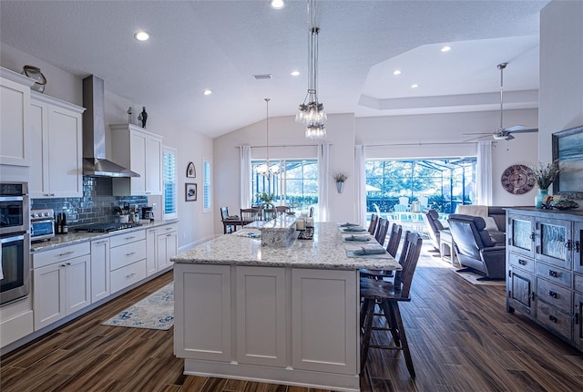 kitchen featuring wall chimney range hood, plenty of natural light, and white cabinets