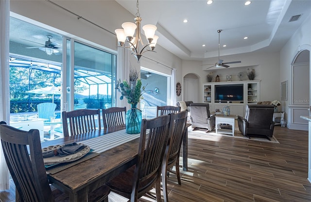 dining space with ceiling fan with notable chandelier, a raised ceiling, and dark hardwood / wood-style floors