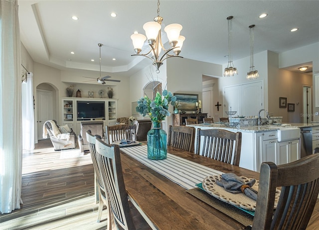 dining room featuring a raised ceiling, light hardwood / wood-style flooring, and ceiling fan with notable chandelier