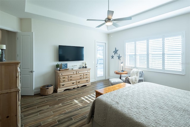 bedroom featuring dark wood-type flooring, a raised ceiling, access to outside, and ceiling fan