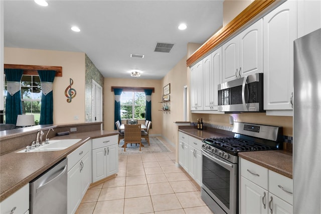 kitchen with appliances with stainless steel finishes, sink, light tile patterned floors, and white cabinets