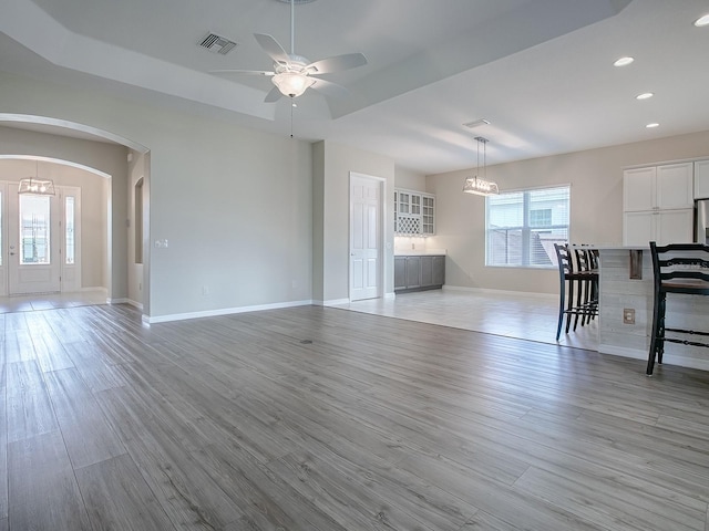 unfurnished living room featuring ceiling fan with notable chandelier and light hardwood / wood-style flooring