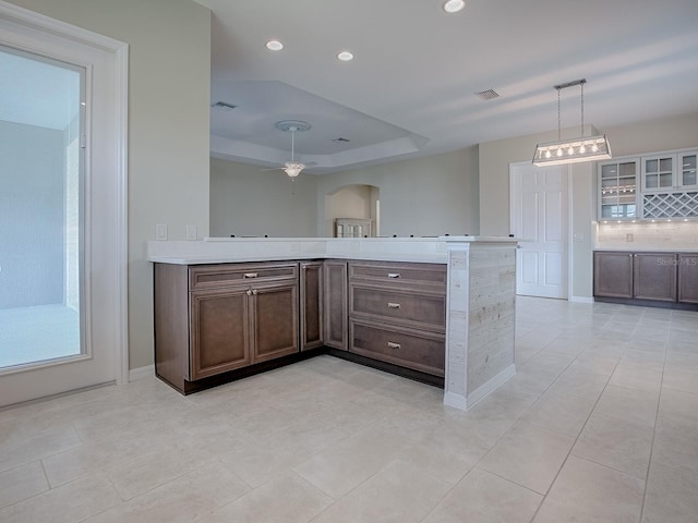 kitchen with light tile patterned flooring, kitchen peninsula, backsplash, dark brown cabinetry, and ceiling fan