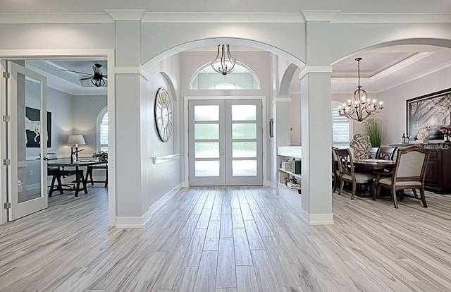 entrance foyer with a tray ceiling, ceiling fan with notable chandelier, light hardwood / wood-style flooring, ornamental molding, and french doors