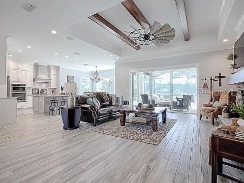 living room with ceiling fan with notable chandelier, beam ceiling, and light hardwood / wood-style floors