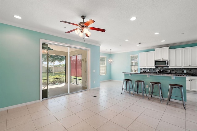 kitchen featuring ceiling fan, a kitchen breakfast bar, backsplash, white cabinets, and ornamental molding