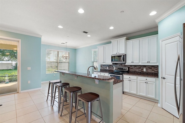 kitchen featuring white cabinets, pendant lighting, stainless steel appliances, and an island with sink