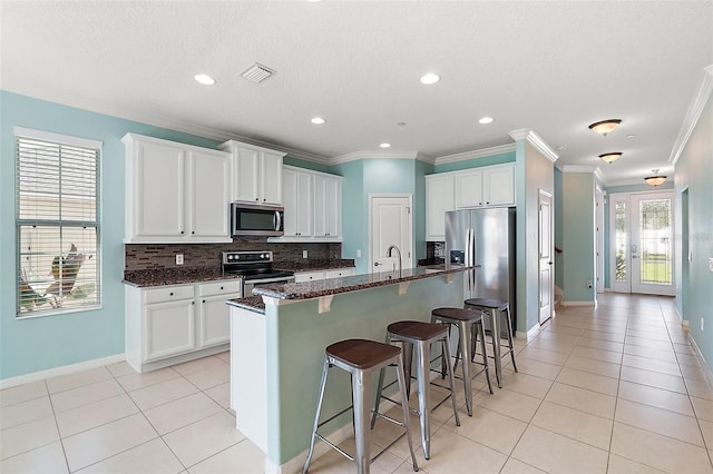 kitchen with dark stone countertops, white cabinetry, an island with sink, and appliances with stainless steel finishes