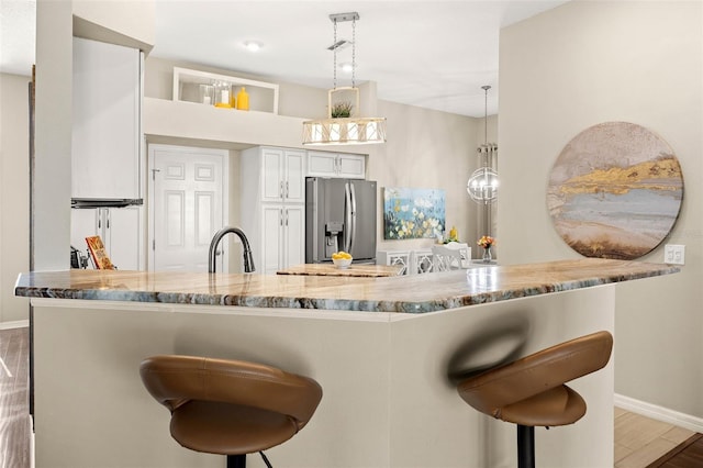 kitchen featuring a breakfast bar, pendant lighting, white cabinets, stainless steel fridge, and kitchen peninsula