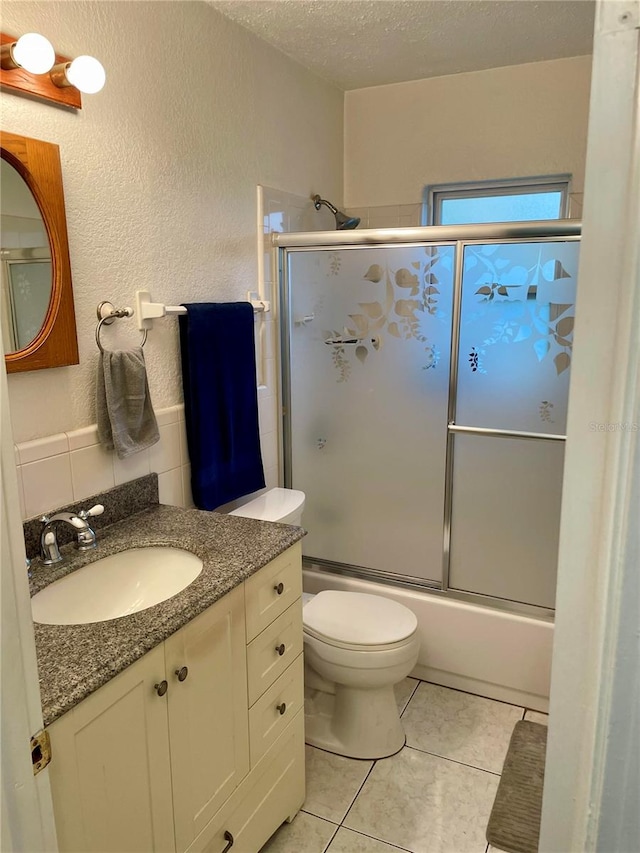 full bathroom featuring vanity, a textured ceiling, combined bath / shower with glass door, toilet, and tile patterned floors