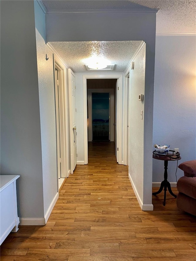 hall featuring a textured ceiling, crown molding, and light hardwood / wood-style floors