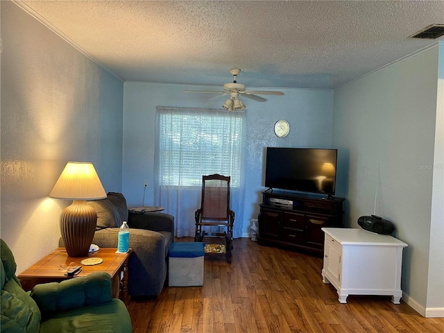 living room featuring ornamental molding, ceiling fan, dark wood-type flooring, and a textured ceiling