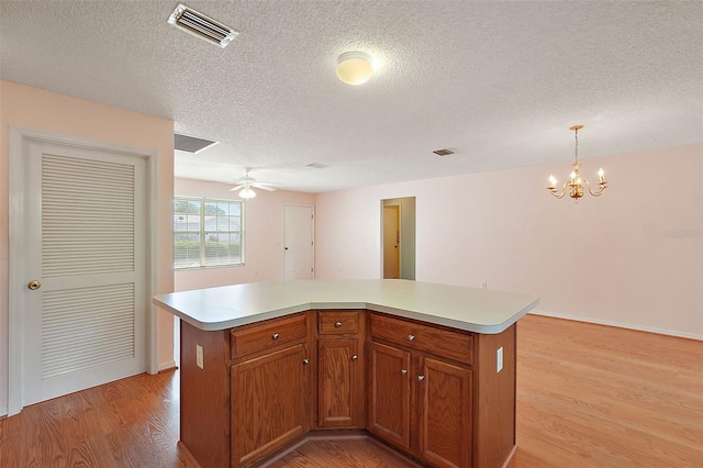 kitchen with ceiling fan with notable chandelier, light wood-type flooring, a textured ceiling, a center island, and decorative light fixtures