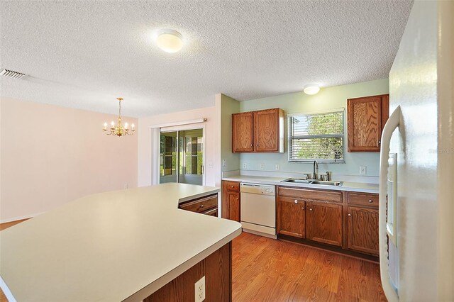 kitchen with hanging light fixtures, white appliances, light wood-type flooring, an inviting chandelier, and sink