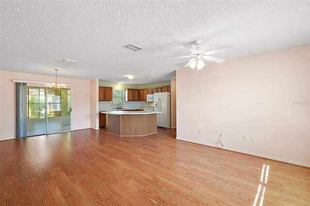 unfurnished living room with ceiling fan with notable chandelier, a textured ceiling, light wood-type flooring, and sink